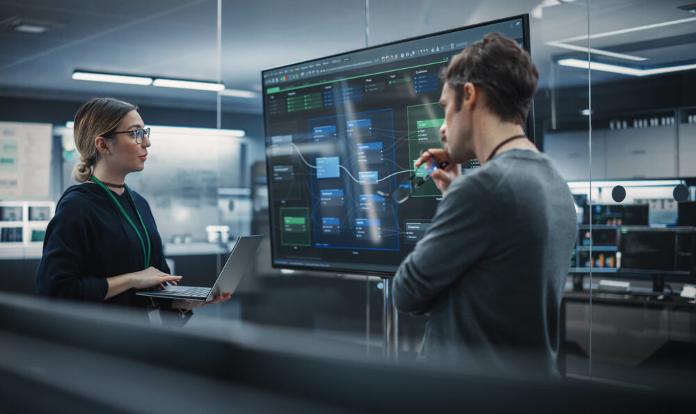 Two Diverse Software Developers Having a Meeting in a Conference Room. Female and Male Tech Industry Engineers Brainstorming Ideas for Their Neural Network Blockchain Startup